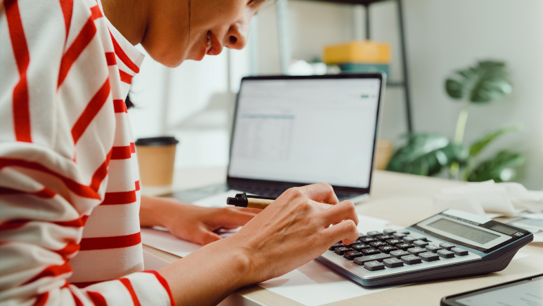 Woman sitting with laptop and using desk calculator