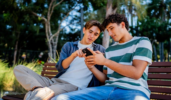 Two people reviewing account information on a mobile banking app while sitting on a park bench.