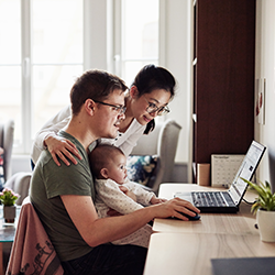 Parents holding baby sitting in front of laptop