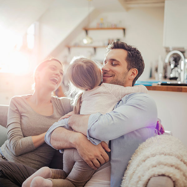 Smiling family on couch hugging young child.